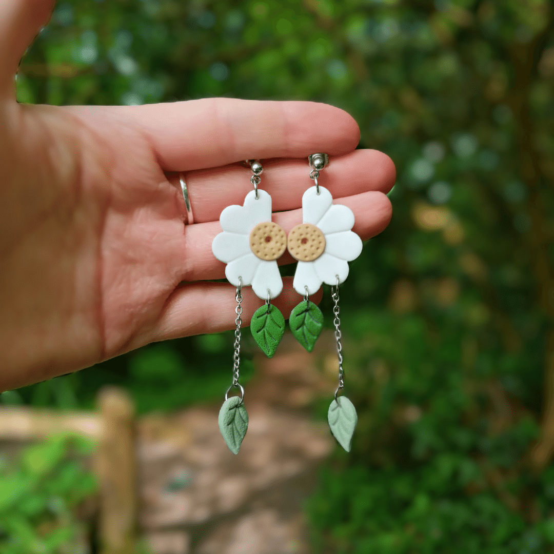 Half Daisy Polymer Clay Statement Drop Studs in Hand for Scale with Nature Background.