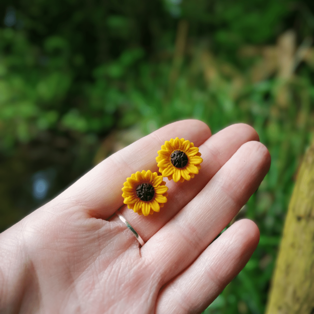 Hand crafted polymer clay Sunflower studs with hand for scale.