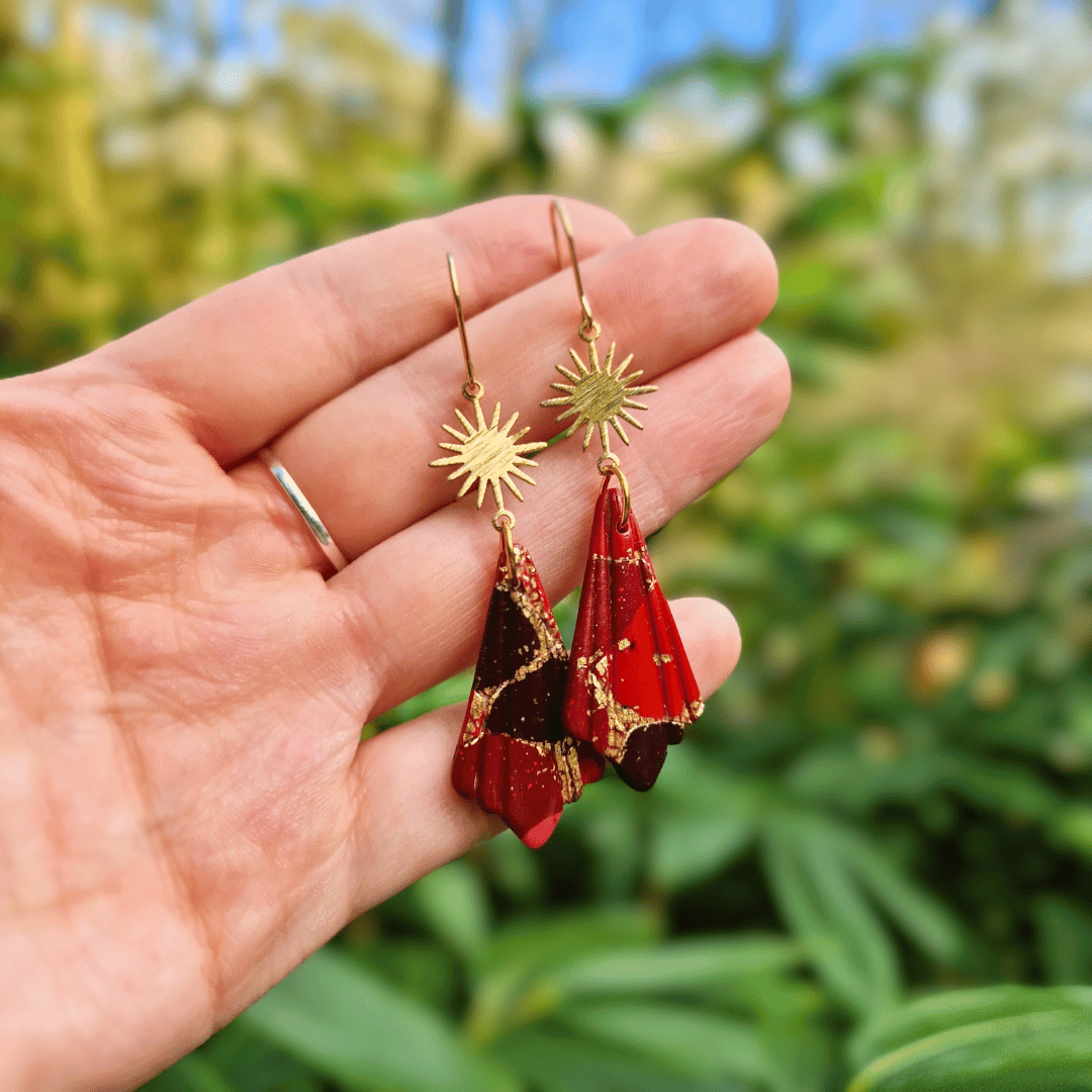 Hand for Scale of our Zero Waste Polymer Clay Sun Hook Earrings with Nature Background.
