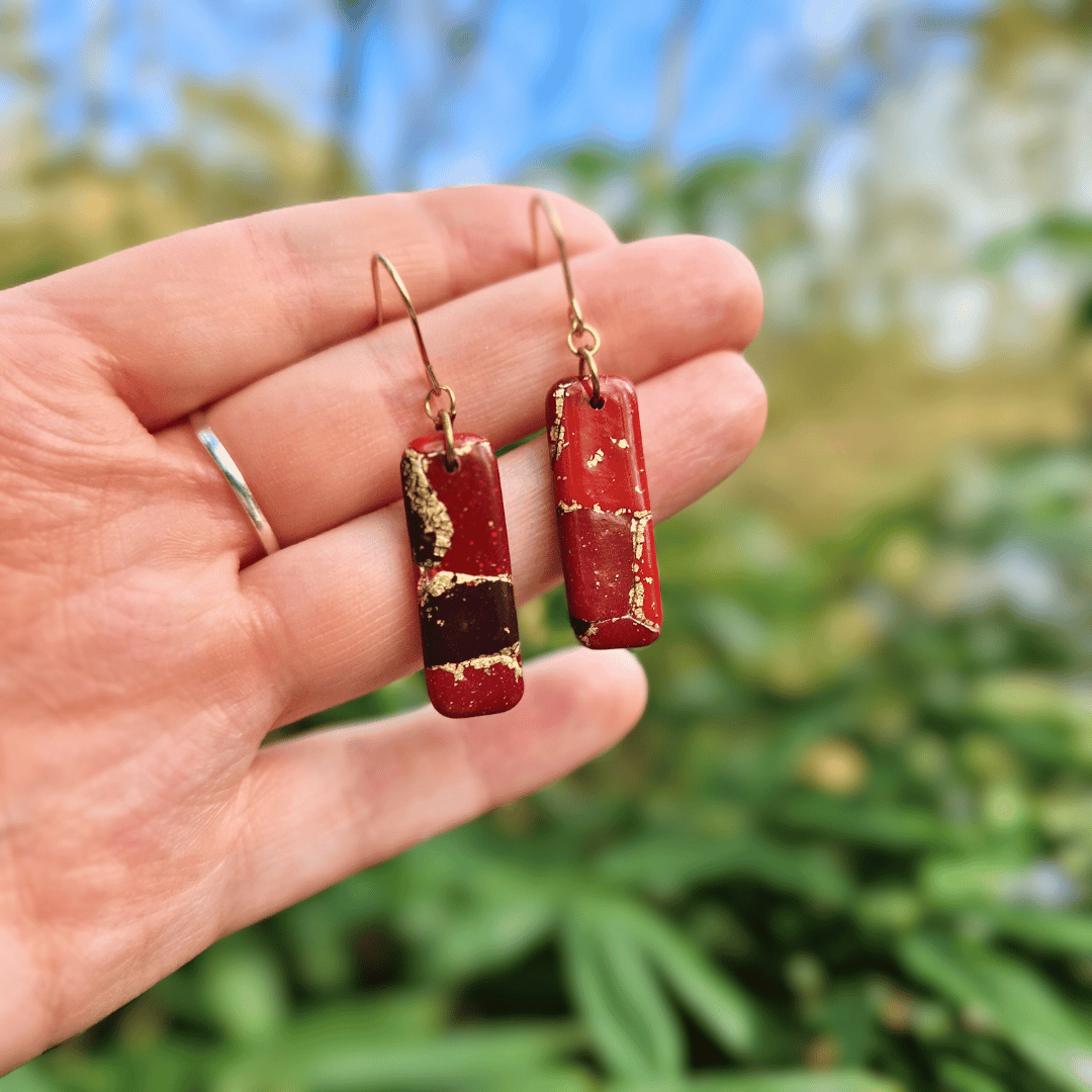 Hand for Scale Image for the Zero Waste Reds and Gold Everyday Hook Earrings with Nature Background.