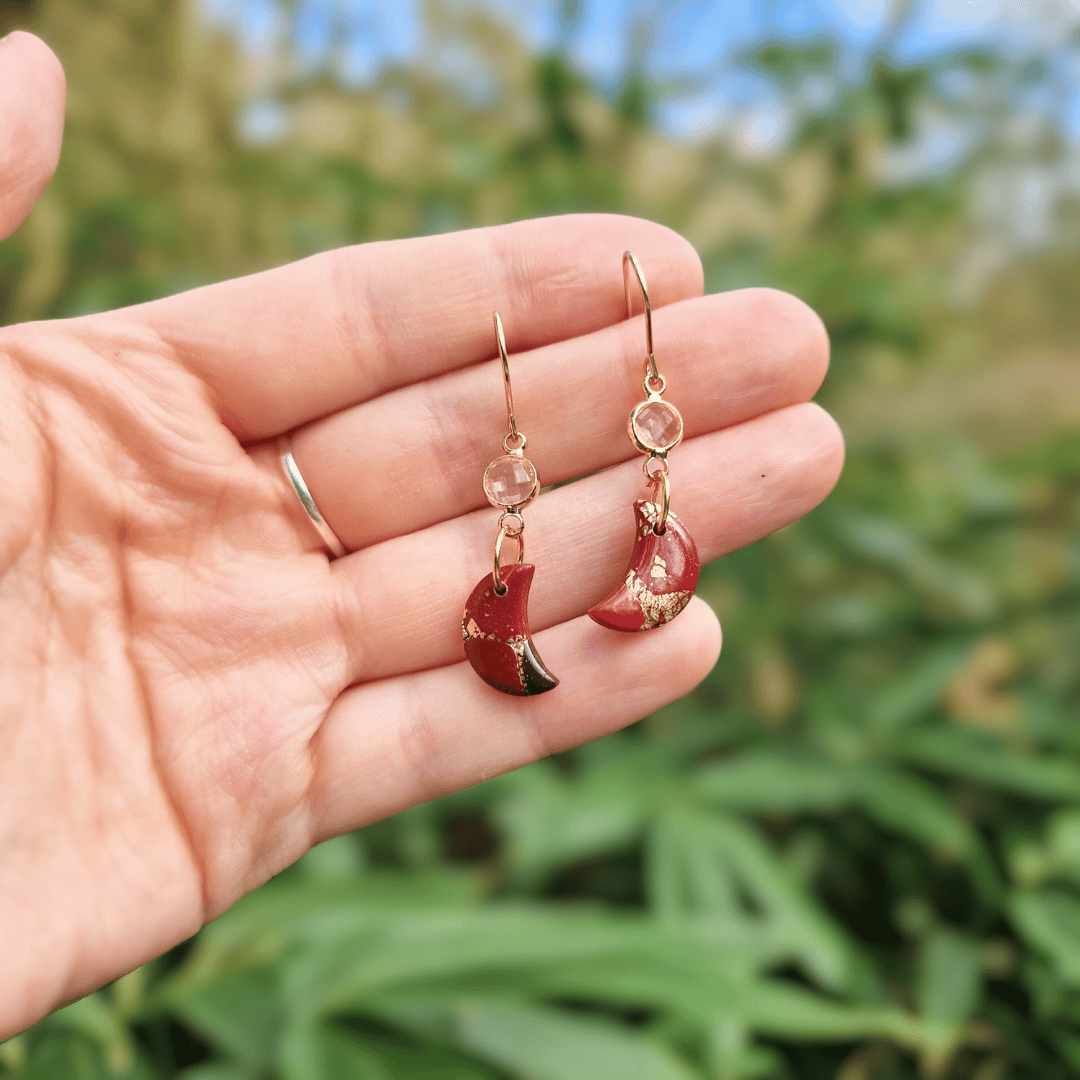 Hand for Scale for Option 1 of the Zero Waste Crescent Moon Red and Gold Earrings in Nature Background.