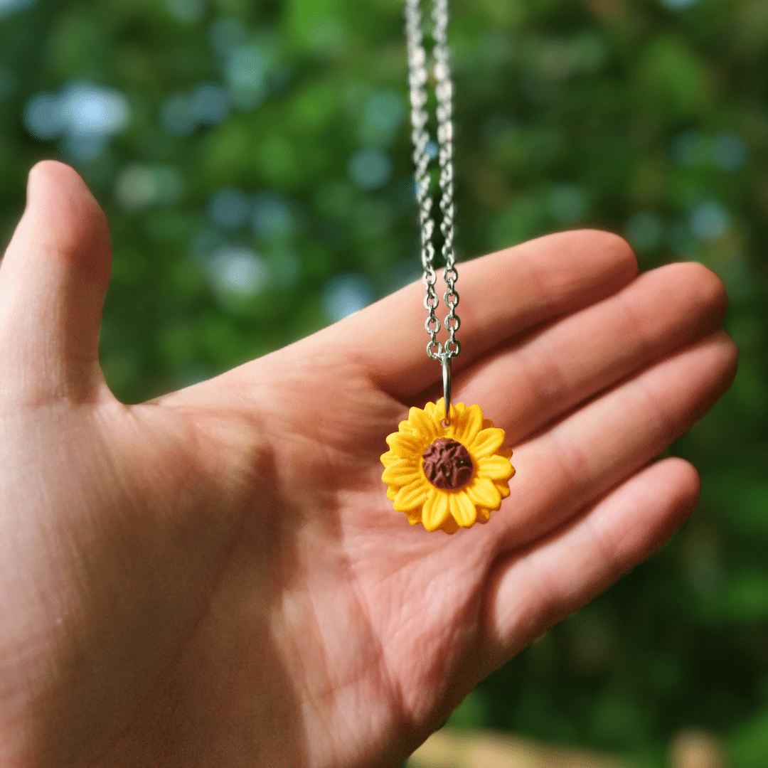 Joyful and intricate polymer clay Sunflower necklace with hand for scale.