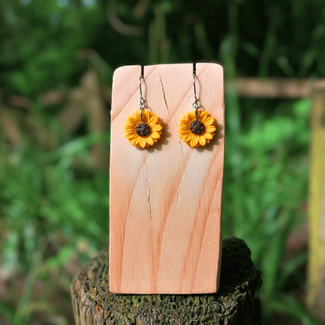 Front view of our polymer clay Sunflower earrings on wooden stand with nature background.