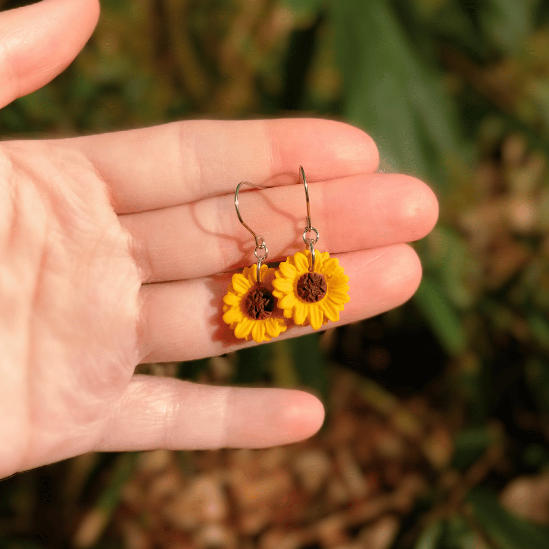 Joyful and detailed polymer clay Sunflower hook earrings with hand for scale.