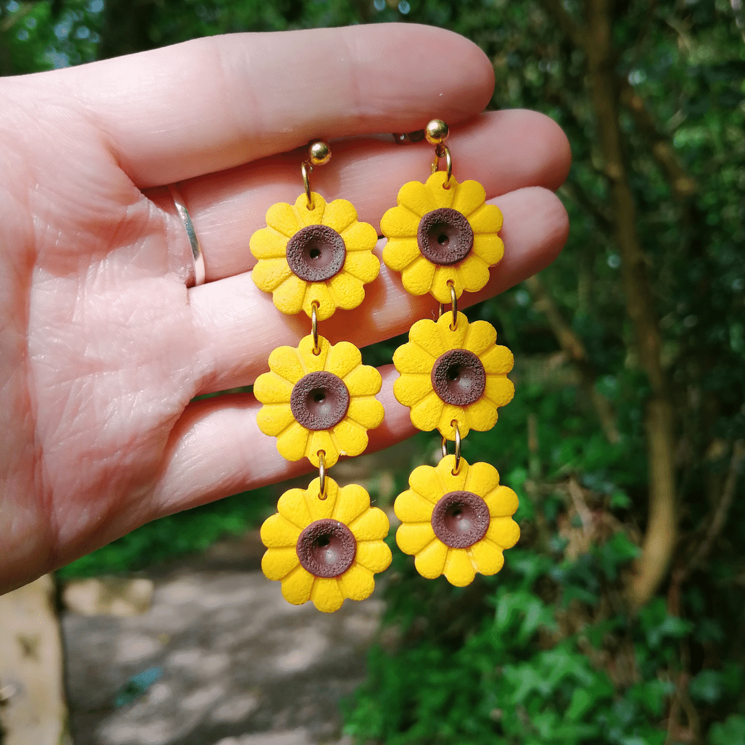 Polymer clay statement Sunflower studs with hand for scale, hand crafted in Dorset.